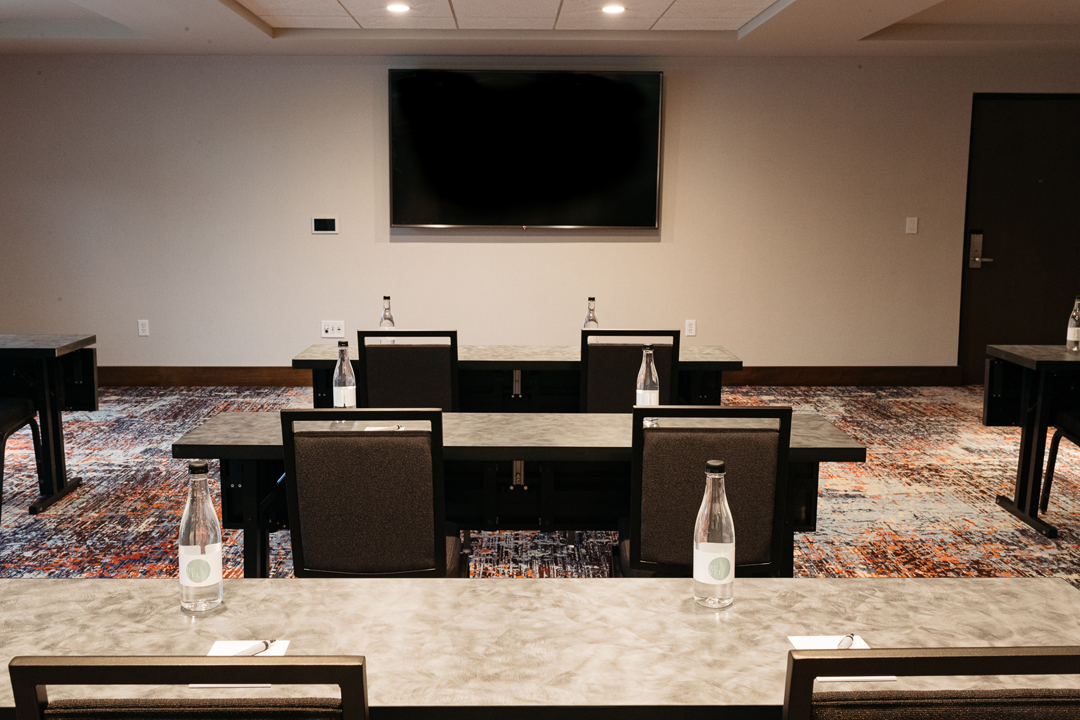 TV hangs on the wall with tables evenly spaced out in the meetings & events space